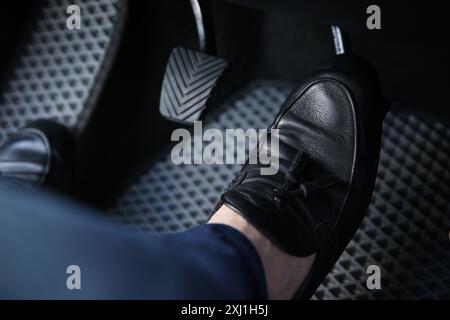 Mann in schwarzen Schuhen, der auf das Pedal der Autobremse drückt, Nahaufnahme Stockfoto