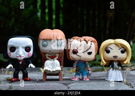 Funko Pop Actionfiguren von bösen Puppen aus Horrorfilmen. Billy die Puppe, Annabelle, Chucky und Tiffany. Dunkler Hof, schwarzer Zaun, stimmungsvolles Grün. Stockfoto