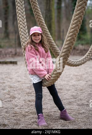 Süßes Mädchen, das Spaß auf einer Kinderschaukel hat. Sitzt auf einem Karussell aus dicken Seilen. Glückliche Kindheit. Stockfoto