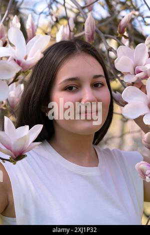 Ein junges Mädchen mit dunklen Haaren in rosa Magnolienblüten. Nahaufnahme. Frühling, Magnolienblüte Stockfoto