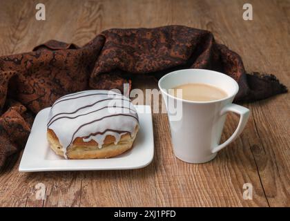 Köstlicher Donut mit Schokolade auf einem weißen Teller und eine Tasse Kaffee auf einem Holztisch. Draufsicht, Kopierraum Stockfoto