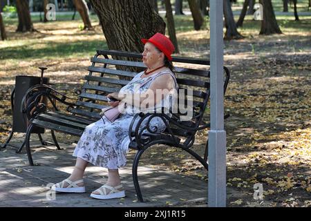 ODESA, UKRAINE - 13. JULI 2024 - eine ältere Frau sitzt auf der Bank im Schatten, Odesa, Süd-Ukraine. Stockfoto