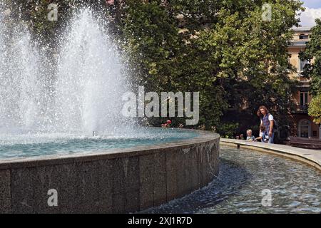 ODESA, UKRAINE - 13. JULI 2024 - Eine Frau und Kinder stehen an einem heißen Sommertag an einem Brunnen in Odesa, Süd-Ukraine. Stockfoto