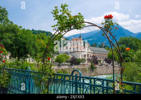 Meran, Südtirol, Italien - Kurhaus am Fluss Passer, an der Passerpromenade in der Altstadt. Vorne Rote Rosen auf der Thermenbrücke. Meran Süddtirol Italien *** Meran, Südtirol, Italien Kurhaus an der Passer-Promenade in der Altstadt Rote Rosen vor der Thermalbrücke Meran Südtirol Italien Stockfoto