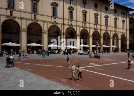 Sonnenschirme und Restauranttische unter dem langen Säulengang, der Loggia oder der Galerie des Palazzo delle Logge, eines von Giorgio Vasari (1511 - 1574) entworfenen Renaissance-Palastes auf der Piazza Grande in Arezzo, Toskana, Italien. Stockfoto