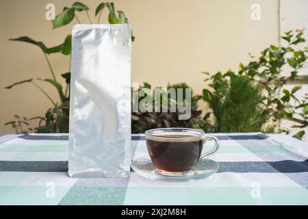 Kaffeebeutel-Paket Mockup mit Espresso Americano und Cofee-Bohnen, gemahlenem Kaffee auf Gartentisch Stockfoto