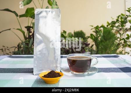 Kaffeebeutel-Paket Mockup mit Espresso Americano und Cofee-Bohnen, gemahlenem Kaffee auf Gartentisch Stockfoto