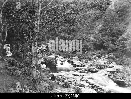 Landschaft des Lyn-Tals. Eine Dame mit einem Sonnenschirm am Fluss Lyn. Lynmouth, Devon. Dieses Foto stammt von einem edwardianischen Original, um 1910. Das Original war Teil eines Albums von 150 Albumenfotos von unterschiedlicher Qualität, von denen ich viele fotografiert habe. Die Sammlung enthielt Bilder vor allem von der Isle of man und der englischen Grafschaft Devonshire. Anmerkungen waren im Album enthalten, aber leider gab es keine genauen Daten. Die Originalfotos waren durchschnittlich 6 x 4 ½ Zoll. Stockfoto