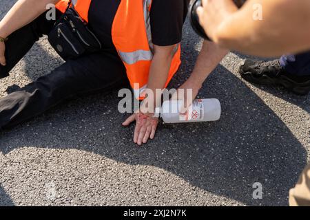 Ein Polizist entfernt die Hand des Aktivisten während der Demonstration vom Asphalt. Menschen in orangefarbenen Westen (Aktivisten der letzten Generation) blockierten den Verkehr auf Aleja Jana Pawla II. Das sind Aktivisten der letzten Generation, die Investitionen in öffentliche Verkehrsmittel fordern. Die letzte Generation blockiert die Hauptarterien Warschaus seit der dritten Woche. Die letzte Generation erklärte vor den Kameras: Wir halten nicht an, unser Ziel ist die längste Reihe ziviler Widerstandskämpfe gegen den Klimawandel in Polen. In der heißesten Jahreszeit sind sich die Menschen der rechtlichen Konsequenzen bewusst Stockfoto