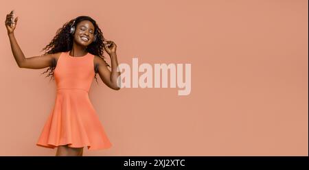 Frau im Orange Kleid tanzt mit Kopfhörern im Studio Stockfoto