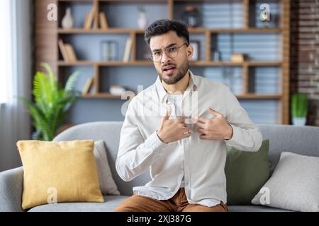Der junge Mann spricht mit dem Arzt per Videoanruf vom Wohnzimmer aus und äußert seine Besorgnis über Brustschmerzen. Das Bild erfasst Telemedizin, Fernkonsultation und Kommunikation zwischen Patient und Arzt Stockfoto