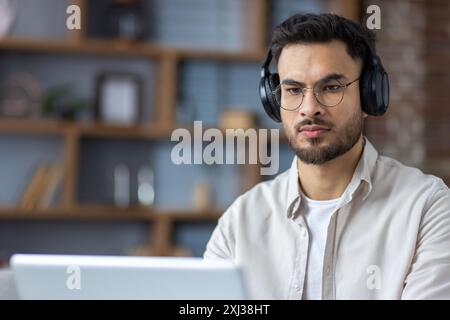 Nahaufnahme eines ernsthaften und fokussierten jungen Indianers mit Kopfhörern, der zu Hause auf einem Laptop arbeitet und studiert. Stockfoto