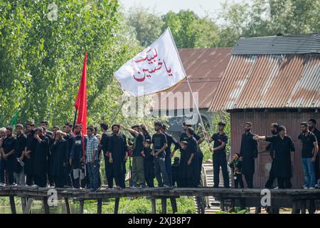 Srinagar, Indien. Juli 2024. Kaschmiri schiitische Trauernde hissen religiöse Fahnen während der Prozession im Inneren des Dal-Sees in Srinagar am 9. Muharram, dem ersten und heiligsten Monat des islamischen Kalenders. Schiitische Muslime gedenken Muharram als einen Monat der Trauer zum Gedenken an das Martyrium des Enkels des islamischen Propheten Muhammad, Imam Hussain, der zusammen mit seinen Familienmitgliedern in der Schlacht von Karbala im südlichen Irak im Jahr 680 n. Chr. getötet wurde Credit: SOPA Images Limited/Alamy Live News Stockfoto