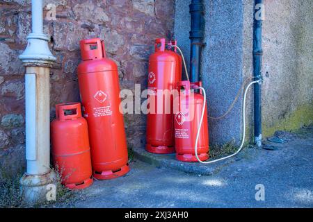 Leuchtend rote Gasflaschen, Gaskannister, die an einer Wand in einer Straße stehen, von Calor Gas Ltd Warwick; einige sind durch Röhren verbunden Stockfoto