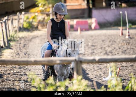 Kind, das Reitunterricht in der Reitschule nimmt. Junge auf Pony mit Schutzhelm. Outdoor-Aktivitäten im Sommer für Kinder. Pferdetraining i Stockfoto