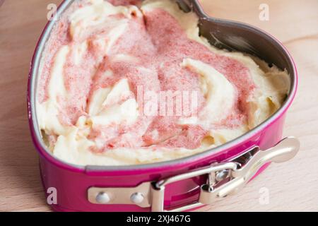 Eine herzförmige pinkfarbene Springform gefüllt mit Teig für einen Erdbeerkuchen. Stockfoto