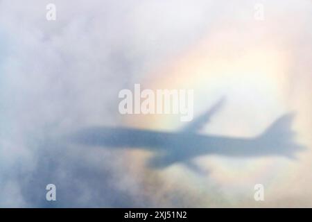 Ein Flugzeug wirft einen Schatten auf eine Wolke, Silhouette, einen Regenbogen. Deutschland Stockfoto