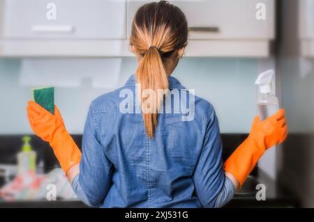 Rückansicht einer asiatischen Frau, die rosa Gummihandschuhe trägt, Lappen und Sprühflasche mit Waschmittel hält, Hände an den Hüften Stockfoto