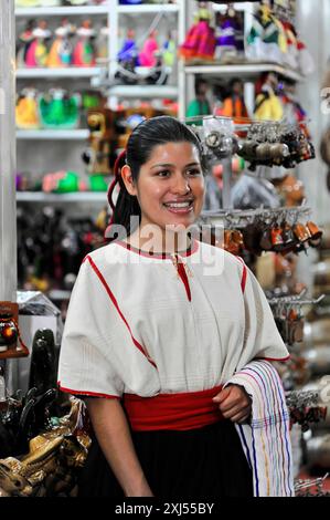 Oaxaca, Mexiko, Mittelamerika, lächelnde Frau in traditioneller Kleidung vor einem Verkaufsstand, in dem buntes Kunsthandwerk und Schmuck verkauft werden Stockfoto