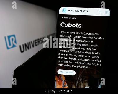 Stuttgart, Deutschland, 02.12.2024: Person, die ein Mobiltelefon mit Website des dänischen Cobot-Unternehmens Universal Robots vor dem Logo hält. Konzentrieren Sie sich auf Stockfoto