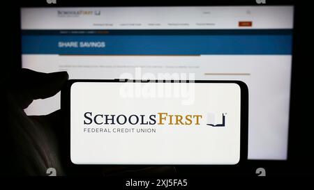 Stuttgart, 23.02.2024: Person mit Mobiltelefon mit Logo des US-Finanzunternehmens SchoolsFirst Federal Credit Union vor der Webseite. Stockfoto