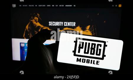 Stuttgart, 22.02.2024: Person, die ein Mobiltelefon mit dem Logo des Battle Royale Videospiels PUBG Mobile vor der Business-Webseite hält. Konzentrieren Sie sich auf Stockfoto