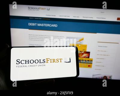 Stuttgart, 23.02.2024: Person mit Smartphone mit Logo des US-Finanzunternehmens SchoolsFirst Federal Credit Union vor der Website. Stockfoto