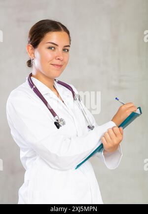 Eine Ärztin macht sich Notizen in Dokumenten, die eine Papiermappe in der Hand haben Stockfoto