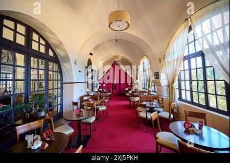 Ein gemütliches Café mit roten Teppichen, Tischen und Stühlen unter Bogenfenstern, die natürliches Licht hereinlassen, Elafos Hotel, Profitis Ilias, Rhodos, Dodecanese Stockfoto