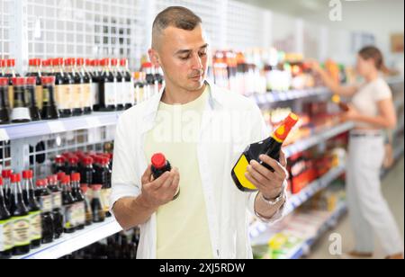 Junger Mann, der Sojasauce im Laden wählt Stockfoto