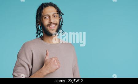 Ein Mann, der mit Daumen nach oben Hand Gesten macht, Zustimmung zeigt, positive Stimmung hat. Fröhliche BIPOC-Person, die Bestätigung vorlegt, Einverständniserklärung macht, Studiohintergrund, Kamera B Stockfoto