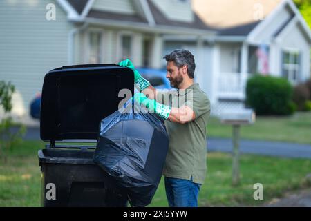 Ein Mann schiebt einen großen Plastikmüll für die wöchentliche Abfallentsorgung. Mann mittleren Alters, der Müll in den Mülltonnen auf der Straße bringt. Mann Stockfoto