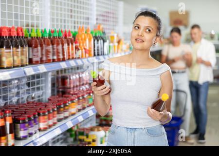 Asiatische Frau liest Etiketten auf Flaschen mit Saucen im Supermarkt Stockfoto