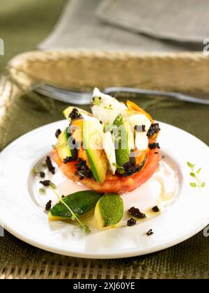 Eine halbe Tomate mit in Scheiben geschnittenem Kabeljau, Zucchinis und schwarzen Oliven Stockfoto