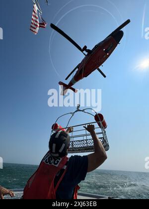 US Coast Guard Academy Kadett 3rd Class Ben Bonetto erhält einen Rettungskorb von einem Air Station Atlantic City MH-65D Dolphin Hubschrauber vor Barnegat Light, New Jersey im Nordatlantik, 15. Juli 2024. Bonetto führte während der Operation ein Training mit zwei separaten MH-65 Dolphin Crews von der Air Station Atlantic City durch. (Foto der US-Küstenwache von Petty Officer 3rd Class Christopher Bokum) Stockfoto