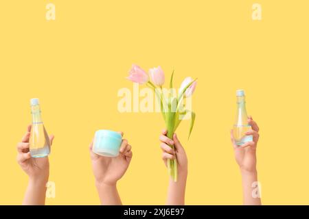 Weibliche Hände mit verschiedenen Kosmetikprodukten und schönen Tulpen auf gelbem Hintergrund Stockfoto