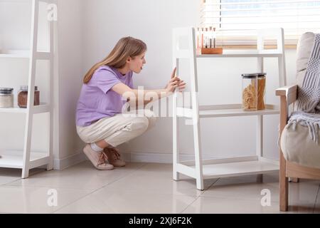 Junge Frau, die zu Hause Schimmel an der Wand in der Nähe des Fensters ansieht Stockfoto