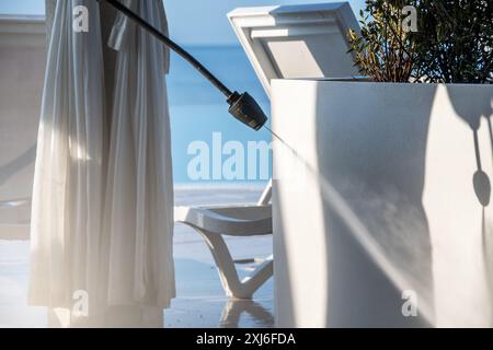 Hochdruckreiniger in Aktion, der an einem klaren sonnigen Tag eine luxuriöse Balkoneinrichtung mit weißen Vorhängen, Stühlen und einer Topfpflanze reinigt. Perfekt für Stockfoto