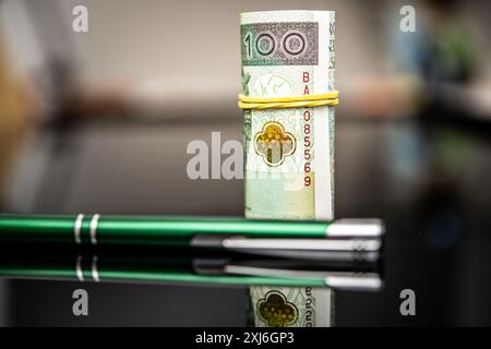100 polnische Zloty gerollt, gesichert mit einem gelben Gummiband, auf einem Satz schlanker grüner Stifte, die Finanztransaktionen oder Vertragsunterzeichnungen darstellen Stockfoto