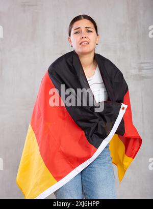 Traurige junge Studentin mit deutscher Flagge vor grauem Wandhintergrund Stockfoto