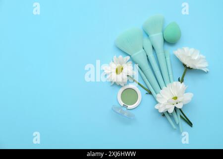 Schöne Komposition mit Blumen, Make-up-Pinseln und Mono-Lidschatten-Palette auf blauem Hintergrund Stockfoto
