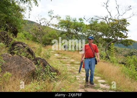 Ein ranghöchster hispanischer Mann, der auf einem ländlichen Pfad läuft, einem restaurierten königlichen Steinweg, der von Barichara nach Guane in Santander, Kolumbien, führt. Konzept: Aktive Touren Stockfoto