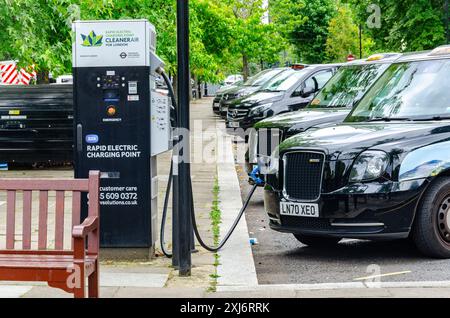 Ein schwarzes Londoner Taxi, das an eine elektrische Schnellladestelle angeschlossen wurde, um auf der Warwick Avenue in London, Großbritannien, aufzuladen Stockfoto