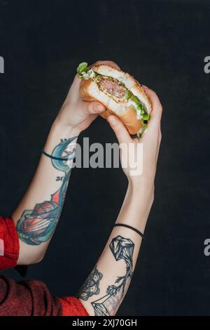 7/8-Ansicht der tätowierte Mädchen essen Hamburger Stockfoto