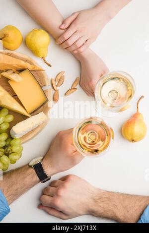 Blick von oben auf die paar mit Weingläsern, verschiedene Sorten Käse, Birnen, Trauben und Mandeln auf Weiß Stockfoto