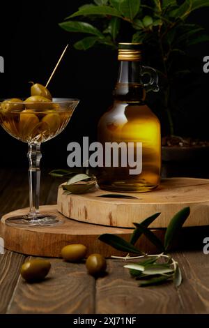 Olivenöl in der Flasche mit Oliven in vintage Glas auf Gestapelte Boards Stockfoto