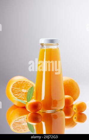 Eine Flasche frischer Orangensaft mit Orangen und kumquats auf eine reflektierende Oberfläche zu richten. Stockfoto