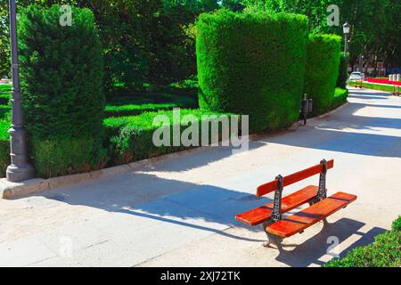 Park mit dekorativen tropischen Büschen in Madrid. Rote Bank auf dem städtischen Bürgersteig im Stadtpark Stockfoto