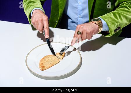 Mann in stilvoller grüner Samtjacke, der Fleischteig auf Teller schneidet Stockfoto