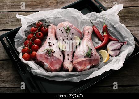 Raw Hähnchenschenkel mit Gewürzen und frischem Gemüse auf Papier auf Auflaufform Stockfoto